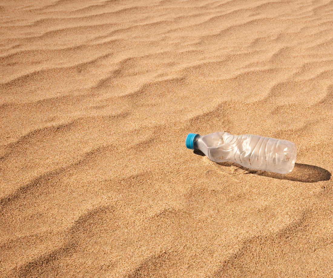 Een leeg plastic flesje op een zandvlakte
