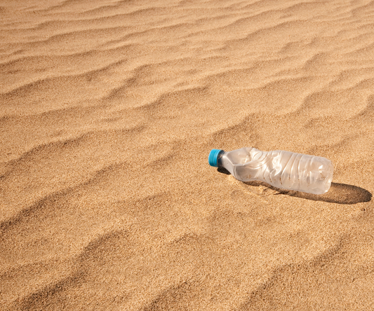 Een leeg plastic flesje op een zandvlakte